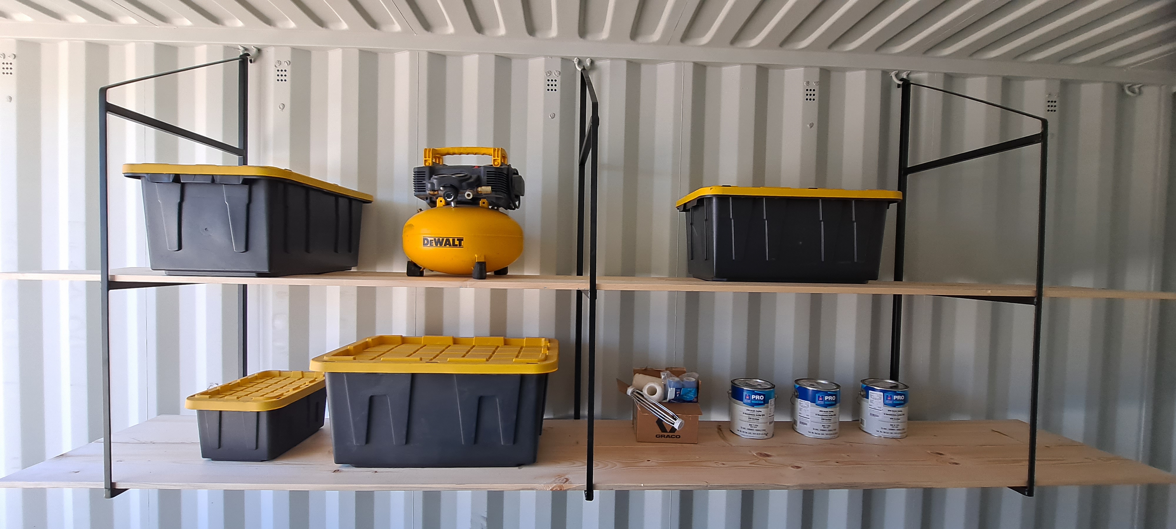 Shelving Bracket Set installed in a shipping container, holding various items including storage bins and a compressor.