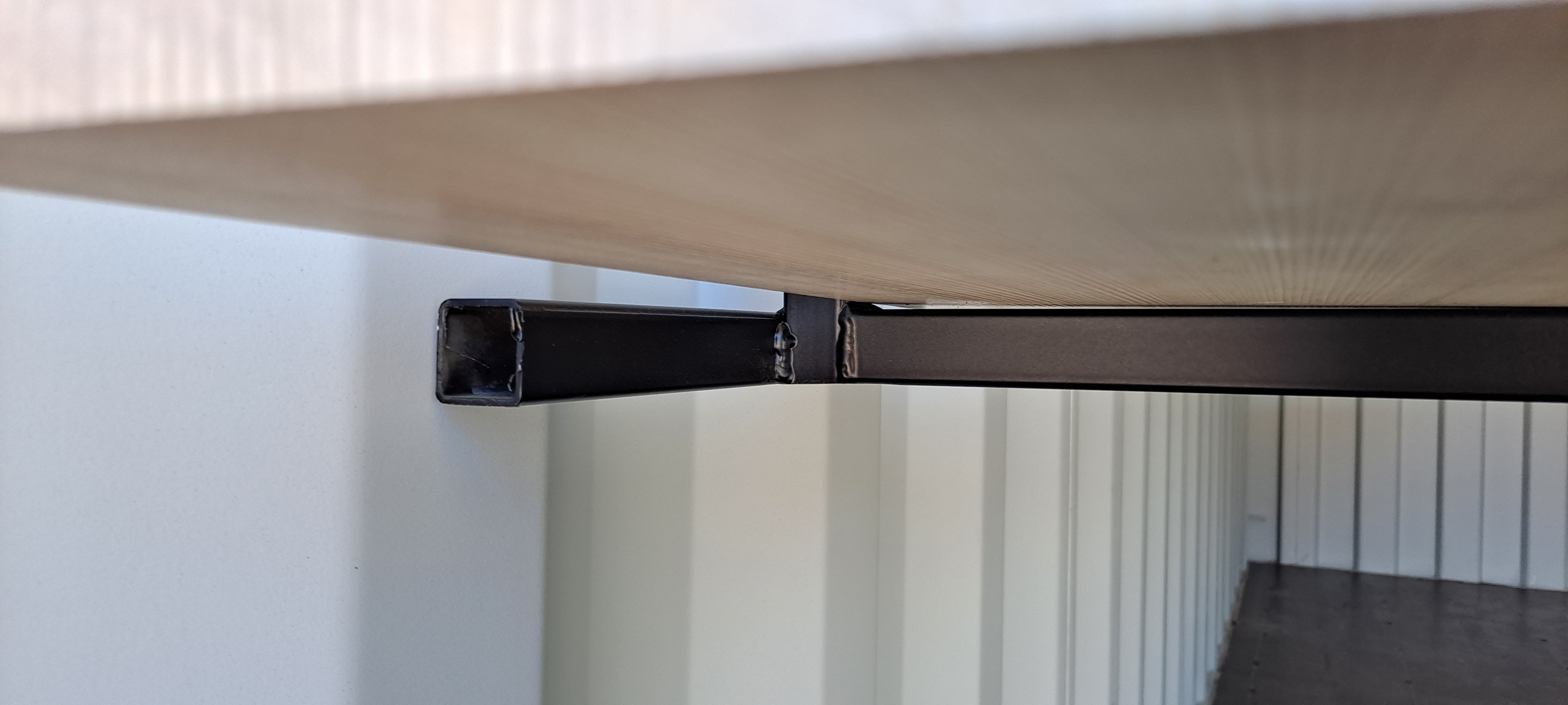 A close-up view of a metal shelving bracket installed in a shipping container, supporting a wooden shelf.